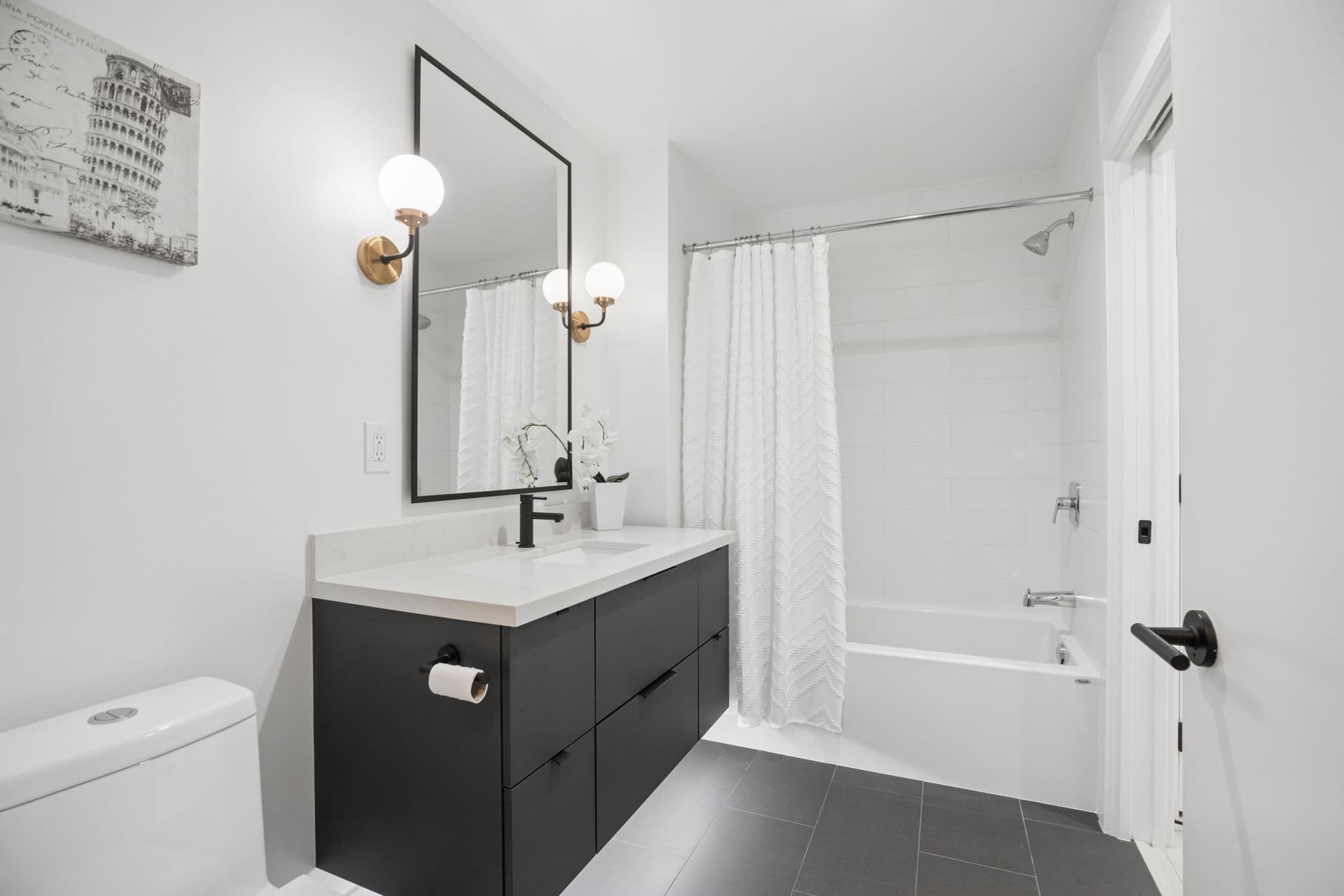 Bathroom with black vanity and brass sconces
